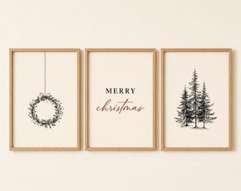 May include: Three framed wall art prints with light wood frames. The left print shows a hanging wreath, the center print features the black and red text Merry Christmas, and the right print displays a black ink illustration of three pine trees.