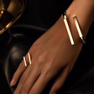 Peut inclure: Un bracelet manchette ouvert doré et une bague ouverte assortie, tous deux dotés d'un design épuré à barres polies. Le bracelet se compose d'une bande incurvée se terminant par deux barres rectangulaires, tandis que la bague reprend ce style.