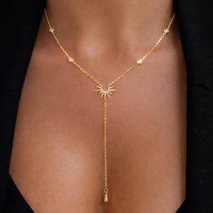 Può includere: Una collana color oro con un ciondolo a forma di raggio di sole e un ciondolo a goccia. La collana presenta piccoli accenti rotondi lungo la catena. Il ciondolo a forma di raggio di sole è incastonato con piccole pietre scintillanti.