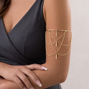 Può includere: Bracciale dorato dal design delicato. La fascia superiore è una semplice barra, con multiple catene a cascata, ognuna ornata da un piccolo ciondolo rettangolare. Questo bracciale è un accessorio elegante.