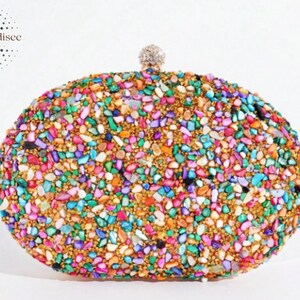 Puede incluir: Bolso de mano ovalado cubierto con un mosaico de piedras coloridas de forma irregular. Las piedras son en tonos rosa, verde, azul y dorado. Un pequeño cierre redondo plateado está en la parte superior. La marca "BagParadisee" está en la esquina superior izquierda.
