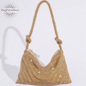 Puede incluir: Un bolso de mano dorado y brillante con un asa anudada. El bolso está cubierto de pequeños adornos brillantes y tiene un cierre de cremallera. El texto "BagParadisee" está en la esquina superior izquierda.