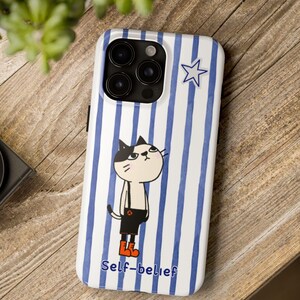 以下が含まれることがあります： 青い縦縞模様の白い携帯電話ケース。漫画の猫のイラストが描かれています。猫は白黒模様で、黒いオーバーオールとオレンジ色のブーツを履いています。猫の上には青い星があり、下には「Self-belief」の文字があります。
