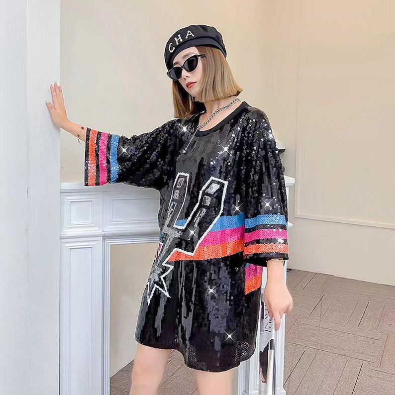 May include: Black sequined dress with a lightning bolt design and colorful stripes on the sleeves. The dress has a loose fit and a round neckline. The sleeves are three-quarter length.