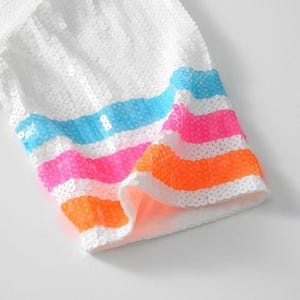 May include: White sequined fabric with colorful horizontal stripes in blue, pink, and orange. The fabric appears to be part of a garment, possibly a sleeve or trim, with a bright and playful design.