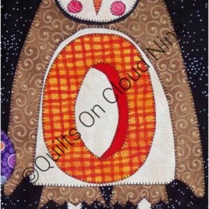May include: A fabric owl appliqué featuring a brown body with swirl patterns, a white face with yellow eyes, and a large orange plaid letter O on its chest. The owl stands on green textured ground against a black background with white dots.