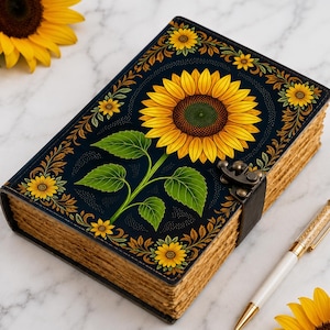 Könnte beinhalten: Ein rechteckiges Tagebuch mit dunkelblauem Einband, verziert mit einer großen gelben Sonnenblumenillustration, grünen Blättern und floralen Bordüren. Das Buch hat einen Metallverschluss, dickes, strukturiertes Papier und einen goldenen Stift.