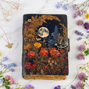 May include: A rectangular journal with a dark blue cover featuring a full moon, pine trees, and various red, orange, and yellow flowers. The journal has a metallic antique-style latch closure and deckled, aged-looking paper edges.
