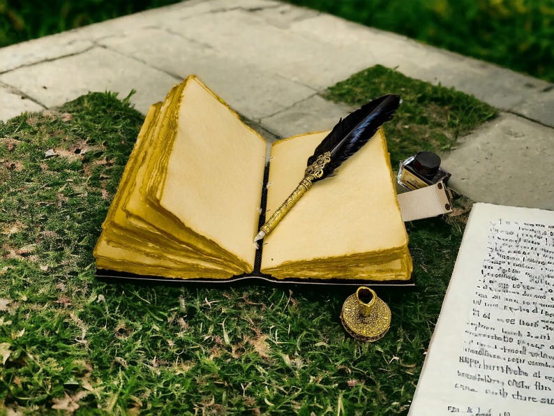 K&ouml;nnte beinhalten: Ein aufgeschlagenes Tagebuch mit dicken, cremefarbenen Seiten und goldfarbenen Kanten. Eine schwarze Feder mit einem verzierten Goldgriff liegt auf den Seiten. Ein kleines Glastintenfa&szlig; und ein rundes Goldsiegel liegen daneben, sowie ein Pergamentblatt.