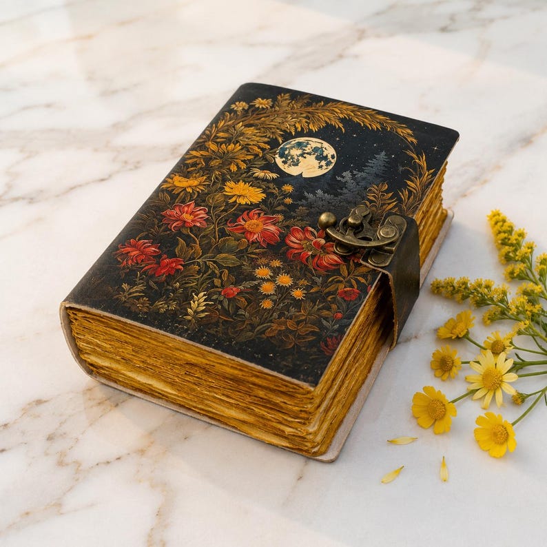 May include: A rectangular journal with a dark cover featuring a full moon, pine trees, and vibrant red and yellow flowers. The book is secured with a metallic latch and has thick, deckled-edge pages with a golden-yellow hue throughout the paper.