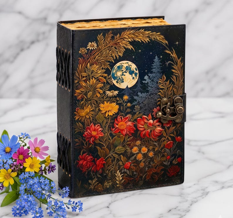 May include: A black hardcover journal featuring a full-color illustration of a night scene with a large moon, pine trees, and vibrant red, yellow, and orange flowers. The book has a metal latch closure and black cord lacing along the spine.