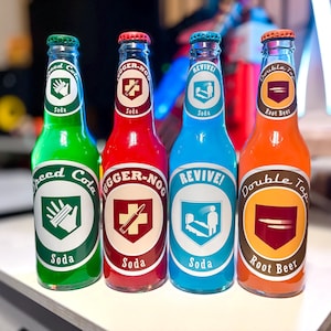 Peut inclure: Quatre bouteilles de soda en verre avec des étiquettes colorées. Les bouteilles sont vertes, rouges, bleues et orange, chacune avec un design d'étiquette et un nom de soda différents. Les étiquettes incluent le texte "Speed Cola", "JUGGER-NOG", "REVIVE!" et "Double Tap Root Beer".