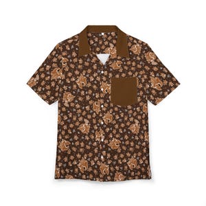 May include: A short-sleeved button-down shirt with a brown floral pattern. The shirt features a dark brown collar and pocket, and a white undershirt is visible. The shirt is made of a lightweight fabric.