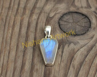 Op de afbeelding: Een zilveren hanger met een rechthoekige, facetgeslepen, blauwe edelsteen. De edelsteen is gezet in een zilveren bezel en heeft een balein voor een ketting. De hanger wordt gepresenteerd op een houten oppervlak.