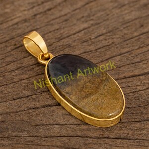 May include: Gold-toned pendant with an oval-shaped stone. The stone transitions from a dark brown to a lighter tan color. The pendant has a loop for a chain and the text "Nishant Artwork" is visible.