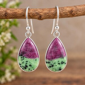 Peut inclure: Une paire de boucles d'oreilles en forme de goutte avec des pierres de rubis zoïsite polies montées sur métal argenté. Chaque boucle possède un crochet arrondi et un sertissage clos encadrant la surface magenta et vert moucheté.