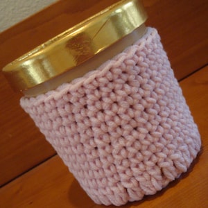 May include: A pink knitted cozy for a to-go cup. The cozy is made with a simple knit stitch and has a gold foil lid on the cup.
