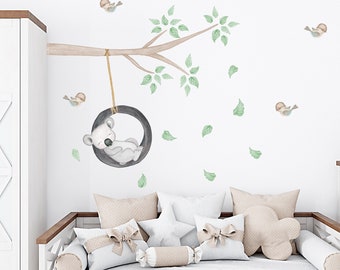 May include: A watercolor-style wall decal featuring a koala bear sleeping on a swing hanging from a tree branch. The decal also includes several small birds and leaves.