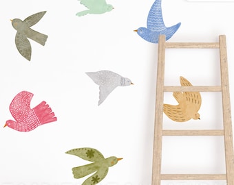 May include: A set of wall decals featuring seven stylized birds in various colors including mint green, olive green, blue, grey, pink, and yellow, alongside a wooden ladder and a white cloud shape, all arranged on a plain white background.