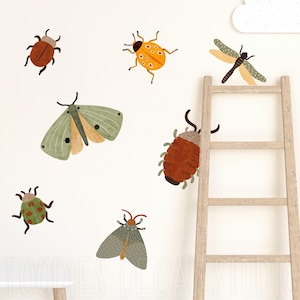 May include: A collection of colorful insect wall decals, including a ladybug, dragonfly, and moth, are displayed on a white wall. A wooden ladder and a cloud-shaped decoration are also visible. The decals are in various shades of brown, green, yellow, and orange.