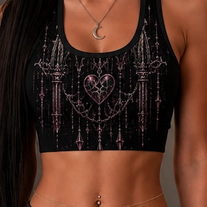 May include: A black racerback sports bra featuring a gothic-inspired print with a central cracked heart, ornate hanging chains, and pointed architectural elements in shades of muted pink and purple, paired with a thin gold waist chain and a moon necklace.
