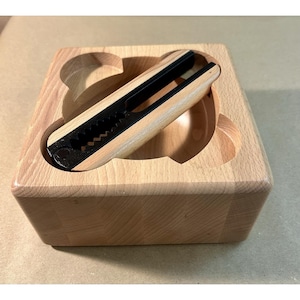 May include: A wooden nutcracker with a black metal cracking mechanism rests in a wooden bear-shaped tray. The nutcracker has a light wood handle and a black, serrated cracking surface. The tray is made of light-colored wood.