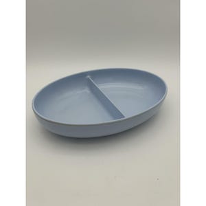 May include: A light blue oval-shaped serving dish featuring a single central divider that splits the interior into two equal sections. The dish has smooth, rounded edges and a solid, matte-finish exterior, providing a clean and functional design.
