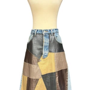 Peut inclure: Jupe patchwork en jean et cuir sur mannequin. La jupe présente une ceinture en jean bleu clair et un motif patchwork de pièces de cuir marron, beige et noir. La jupe a un ourlet effiloché.