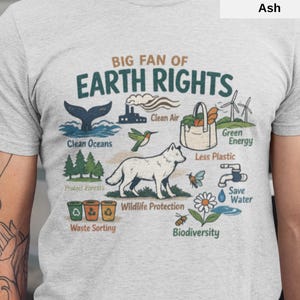 Op de afbeelding: Asgrijze t-shirt met een grafisch ontwerp dat milieubescherming promoot. Het ontwerp bevat illustraties van een walvisstaart, bomen, een wolf en de tekst "Big Fan of Earth Rights", "Clean Oceans" en "Wildlife Protection".