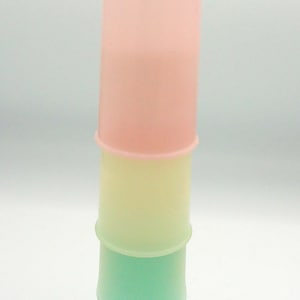 May include: A tower of four pastel-coloured cups. The top cup is a soft pink, followed by yellow, then green, and finally a teal-coloured cup at the bottom. The cylindrical cups are stacked on top of each other, creating a colourful display.
