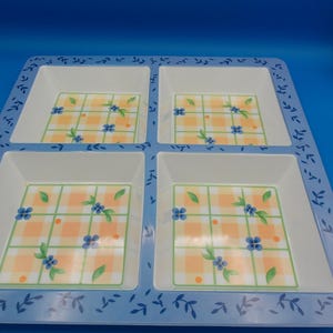 May include: A square serving tray with four compartments. The tray has a light blue border with a leaf design. Each compartment has a white interior and a checkered pattern with blue flowers and green leaves.