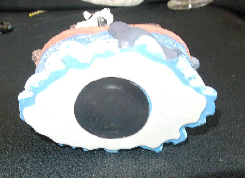 May include: A ceramic coin bank shaped like a seascape, featuring a white and blue design with a whale and a dog figurine. The bank has a large, black coin slot and is painted with various colors.