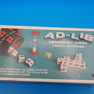 May include: A rectangular game box for Ad-Lib Crossword Cubes, formerly Scribbage. The teal box features a dark green cup, a red hourglass timer, and white lettered cubes. Text includes game instructions and the E.S. Lowe brand logo.