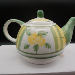 May include: A ceramic teapot featuring a white base with vertical yellow and green stripes. The body is decorated with a hand-painted yellow rose motif surrounded by green leaves. It includes a matching lid with a green knob and a curved spout.