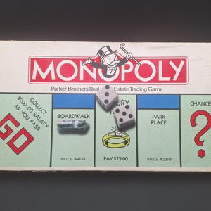 May include: Monopoly board game with dice. The board features the Monopoly logo, property spaces like Boardwalk and Park Place, and the Chance space. The dice show various numbers, and the game is by Parker Brothers.