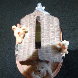 May include: A decorative Noah's Ark figurine with a brown, textured roof and wooden sides. A giraffe, a bear, and a cow peek out from the ark. The ark has a gray animal figure on top.