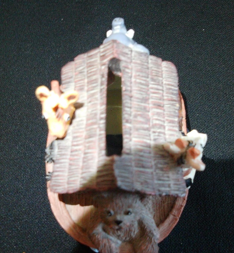 May include: A decorative Noah's Ark figurine with a brown, textured roof and wooden sides. A giraffe, a bear, and a cow peek out from the ark. The ark has a gray animal figure on top.