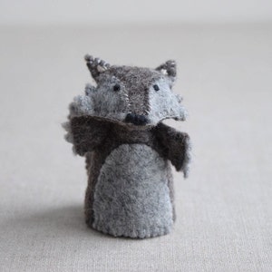 May include: A gray felt finger puppet shaped like a wolf with black eyes and a black nose. The wolf has a gray felt belly and brown felt fur.