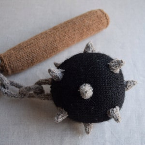 Könnte beinhalten: Eine gestrickte schwarze und graue Stachelkugel, die an einem braunen Strickgriff mit einer grauen Kette befestigt ist.