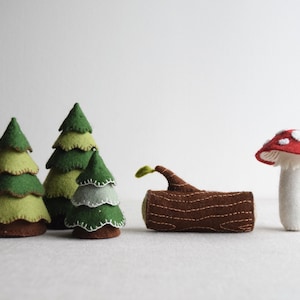 May include: Felt woodland scene with three green trees, a brown log with a green sprout, and a red and white mushroom.