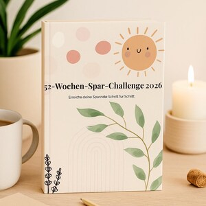 Könnte beinhalten: Ein beiger 52-Wochen-Spar-Challenge 2026-Planer mit einer Sonnenillustration und dem Text "52-Wochen-Spar-Challenge 2026". Der Planer hat ein florales Design und liegt auf einer Holzoberfläche.