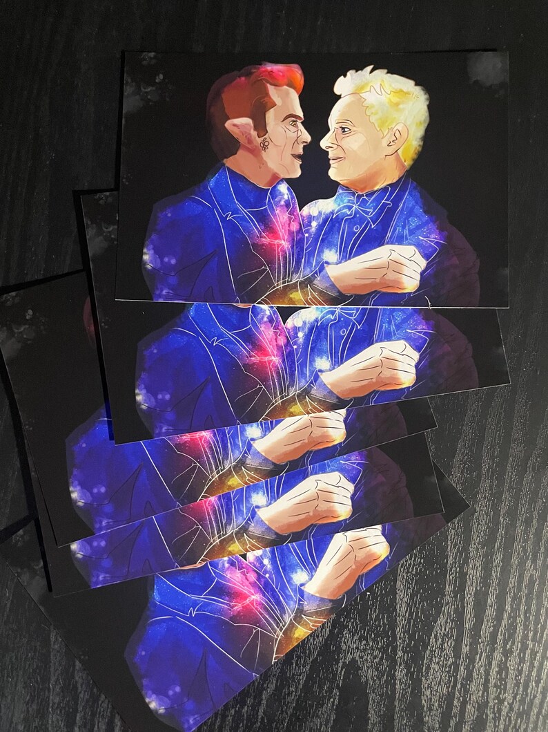 May include: A stack of rectangular art prints featuring a digital illustration of two figures facing each other. The figures are dressed in dark blue suits with a vibrant galaxy pattern of purple, blue, and red nebula clouds across their clothing.