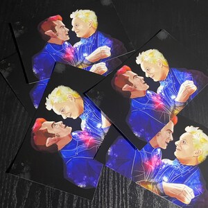 May include: A collection of rectangular art prints featuring a digital illustration of two figures facing each other. One figure has reddish hair and pointed ears, while the other has blonde hair. Both wear dark blue outfits with cosmic patterns.