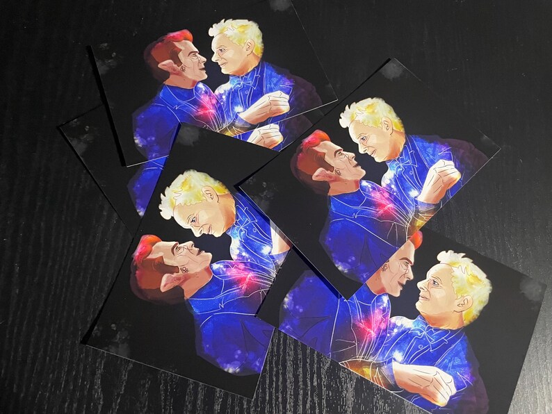May include: A collection of rectangular art prints featuring a digital illustration of two figures facing each other. One figure has reddish hair and pointed ears, while the other has blonde hair. Both wear dark blue outfits with cosmic patterns.