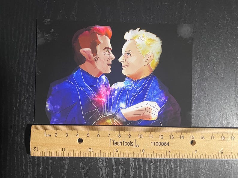 May include: A rectangular art print featuring a digital illustration of two figures facing each other, set against a dark background. The figures wear blue suits with galaxy patterns. A wooden ruler is placed below, showing a width of 20 cm.