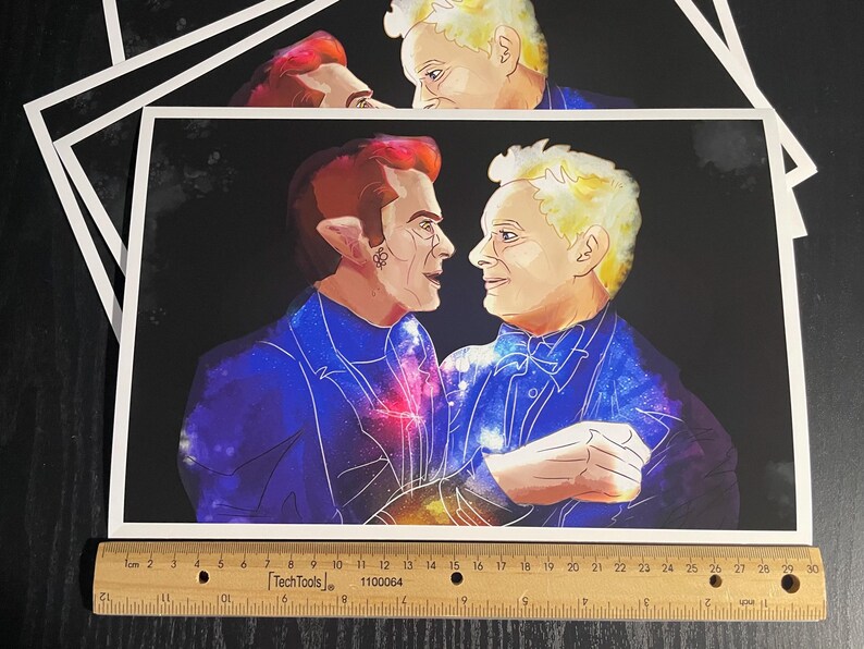 May include: A rectangular art print featuring a digital illustration of two figures facing each other, set against a dark background. The figures wear blue suits with galaxy patterns. A wooden ruler measuring 30 cm is placed along the bottom edge.