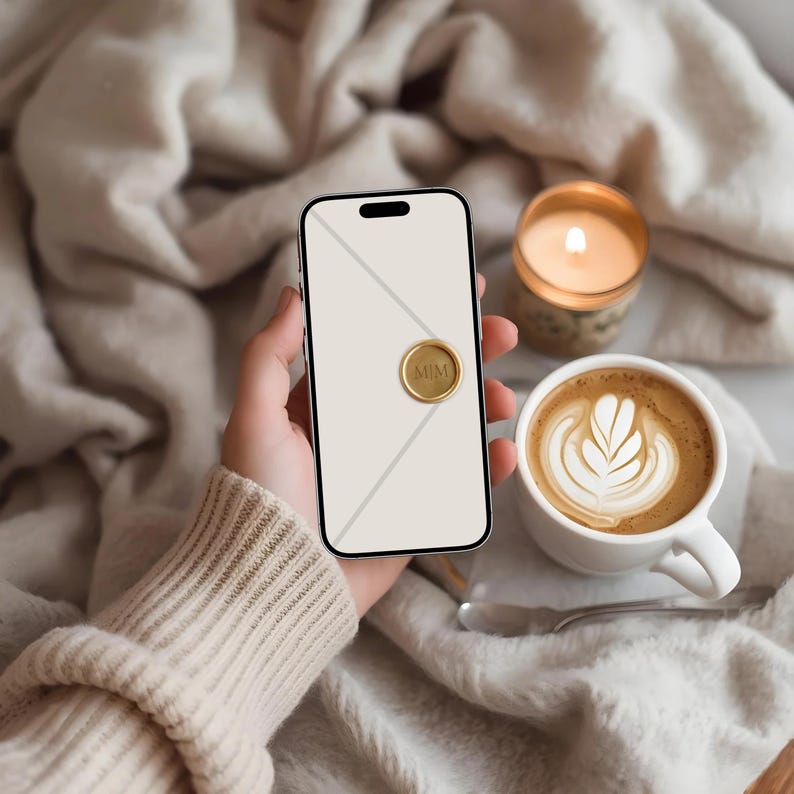 May include: A smartphone with a gold seal that reads "MIM" is held in a hand. A cup of coffee with latte art and a lit candle are next to the phone. The background is a soft, neutral-toned blanket.