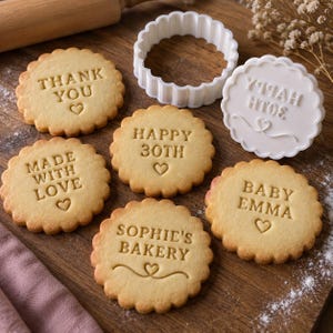 Può includere: Biscotti rotondi con bordo smerlato e un timbro in plastica bianca. I biscotti presentano testi in rilievo tra cui THANK YOU, HAPPY 30TH, MADE WITH LOVE, BABY EMMA e SOPHIE'S BAKERY, ognuno con un piccolo cuore. Il timbro mostra HAPPY 30TH.