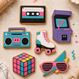 Può includere: Una collezione di sei biscotti a forma di icone degli anni '80, tra cui una cassetta nera, un cabinato arcade viola con uno schermo a forma di cuore, un boombox turchese, un pattino a rotelle bianco, un cubo colorato e occhiali rosa.