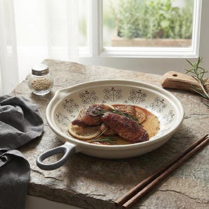 Puede incluir: Un plato de servir color crema con un asa gris, lleno de comida cocinada y rodajas de limón. El plato tiene un patrón floral alrededor del borde. También hay un salero de vidrio y palillos de madera.
